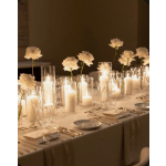 White flowers in glass cylinders with lit candles on a banquet table