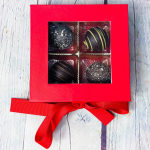 Red gift box with window showing four chocolate truffles and a red ribbon bow.