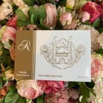 Box of milk chocolates resting on a pink and cream flower arrangement