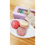 Gift box of assorted macarons with three colorful macarons on a white plate and a kraft gift tag
