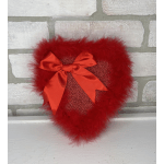 Red heart-shaped decorative pillow with feather trim and satin bow on a light brick background