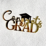 Gold "Congrats Grad" sign with a graduation cap on a textured white background