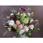 Mixed bouquet of roses, lilies, and purple blooms in a green vase