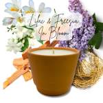 Scented candle in a tan ceramic pot with lilac and white freesia flowers behind it