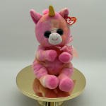 Pink unicorn plush toy with a gold horn and ribbon on a round gold stand