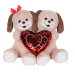 Two plush dogs holding a red heart pillow