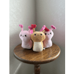 Three plush snail toys with heart-tipped antennae on a wooden table