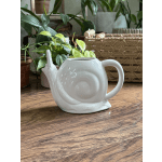 White ceramic snail-shaped watering can on a wooden surface