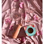 Pink glass coupe and bowl with packaged flower petals on pink fabric with scattered rose petals