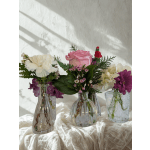 Three small flower arrangements in glass vases with pink, white, and purple blooms