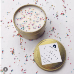 Two gold tin candles on a white surface with colorful sprinkles