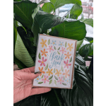 Hand holding a thank you card in front of large green leaves