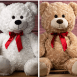 Two plush teddy bears with red ribbon bows, one white and one tan.