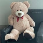 Large beige teddy bear with a red ribbon sitting on a dark chair