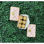 Pink gift boxes with gold trim and chocolates on a green leafy background
