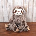 Fluffy brown sloth plush toy sitting on a wooden surface with a rustic wood backdrop