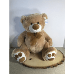 Large tan teddy bear with a brown ribbon sitting on a wood slice