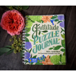 Pink flower beside a gratitude puzzle journal on a dark surface