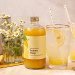 Bottle of lemon mixer beside a glass of lemonade and a jar of daisies