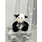 Plush cow toy with a checkered bow sitting on a decorative pedestal