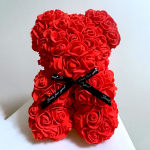 Red artificial rose teddy bear with a black ribbon on a white surface
