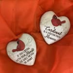 Two heart-shaped memorial stones with cardinal designs on orange fabric.