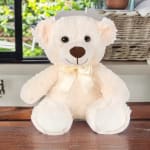 Cream teddy bear with a satin bow sitting on a wooden surface