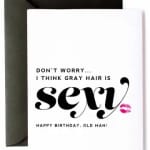White birthday card with bold black “sexy” text, pink lipstick kiss, and a dark envelope behind it.