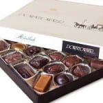 Open box of assorted chocolates in a cream and black gift box.
