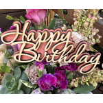 Birthday sign over a mixed floral arrangement with pink and purple blooms