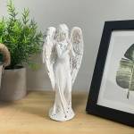 White angel figurine standing on a tabletop beside a framed print and potted plant.