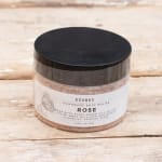 Jar of rose body polish with a black lid on a wooden surface