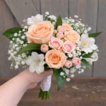 Handheld bouquet of peach and pink roses with white filler flowers