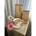 Floral teacup and saucer with pink and white daisies beside two paper coffee bags