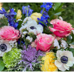 Colorful arrangement with pink roses, white anemones, blue delphinium, and other mixed blooms.