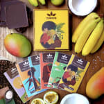 Assorted chocolate bars arranged with tropical fruits on a wooden surface.