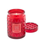 Red glass jar candle with a lit wick and matching lid