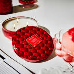 Red decorative candle tin with three wicks on a white surface