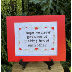 Framed cross-stitch sign with a red border and a heart-themed quote
