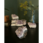 Amethyst crystal clusters on a dark surface with a glass vase of greenery