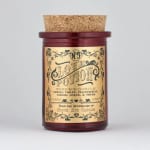 Red glass candle jar with a cork lid and ornate label