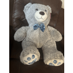 Gray teddy bear with a blue bow sitting on a dark chair