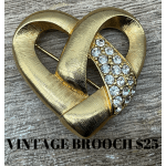 Gold heart-shaped brooch with clear rhinestones on a wood surface