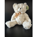 Cream-colored teddy bear with a satin ribbon sitting on a dark surface