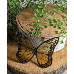 Butterfly ornament in front of a rustic wood slice with trailing greenery