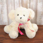 Cream plush puppy with a pink ribbon sitting on a wooden surface