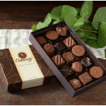 Box of assorted chocolates beside green leaves on a wooden table