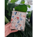 Hand holding a floral butterfly greeting card in front of large green leaves