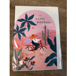 Illustrated Happy Birthday card with a person riding a bicycle through a pink desert scene