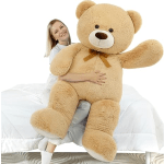 Woman holding a giant tan teddy bear on a bed